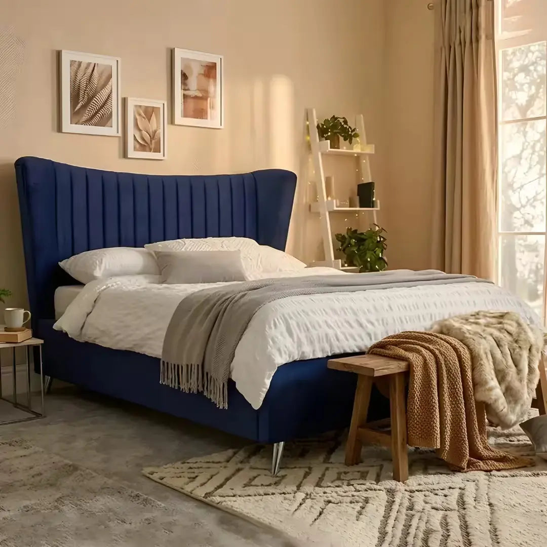 Royal blue velvet upholstered bed frame with winged headboard in a cozy, neutral-toned bedroom with a wooden bench and ladder shelf